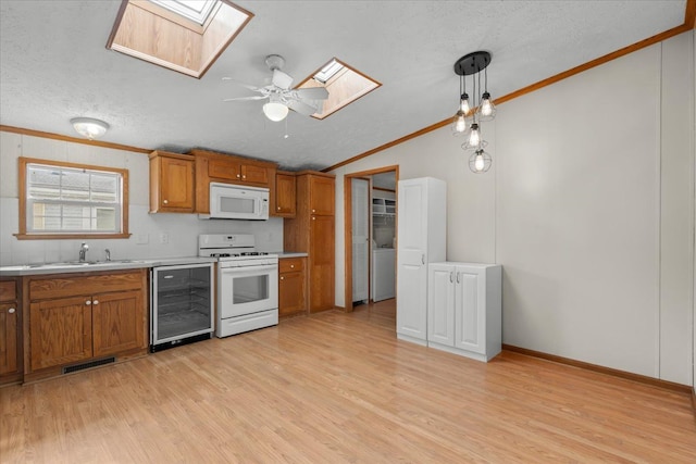 kitchen with white appliances, brown cabinetry, beverage cooler, a sink, and crown molding