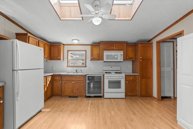 kitchen with crown molding, wine cooler, brown cabinets, a skylight, and white appliances