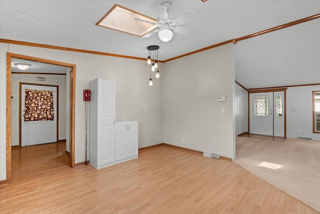 unfurnished room featuring a ceiling fan, visible vents, light wood-style flooring, a skylight, and ornamental molding