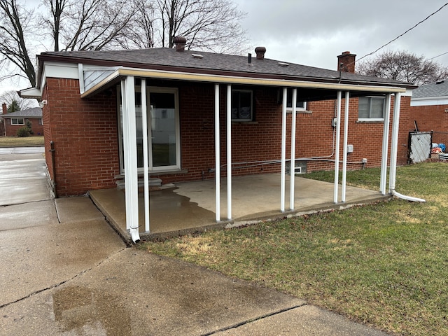 back of property with a yard, brick siding, a chimney, and a patio area