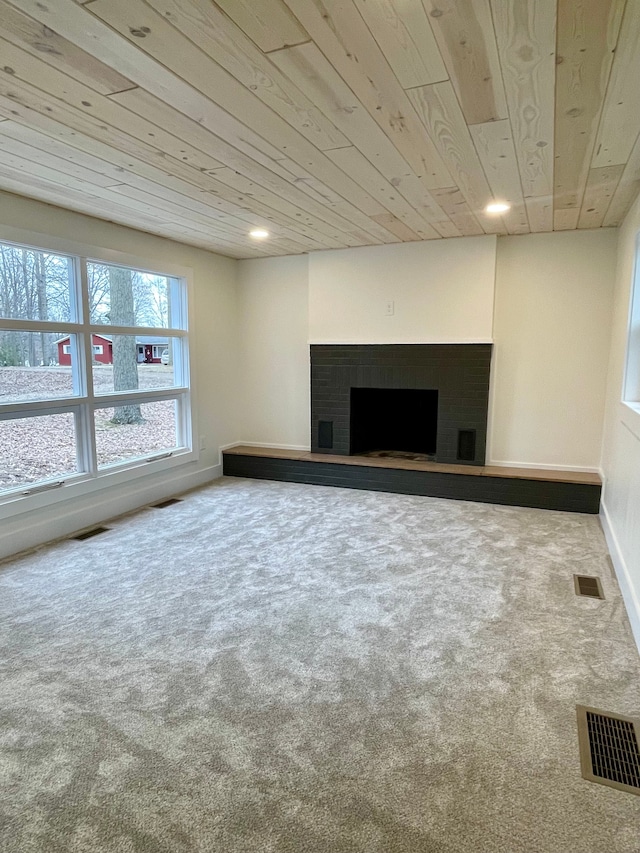 unfurnished living room featuring visible vents, a fireplace with raised hearth, wood ceiling, and carpet