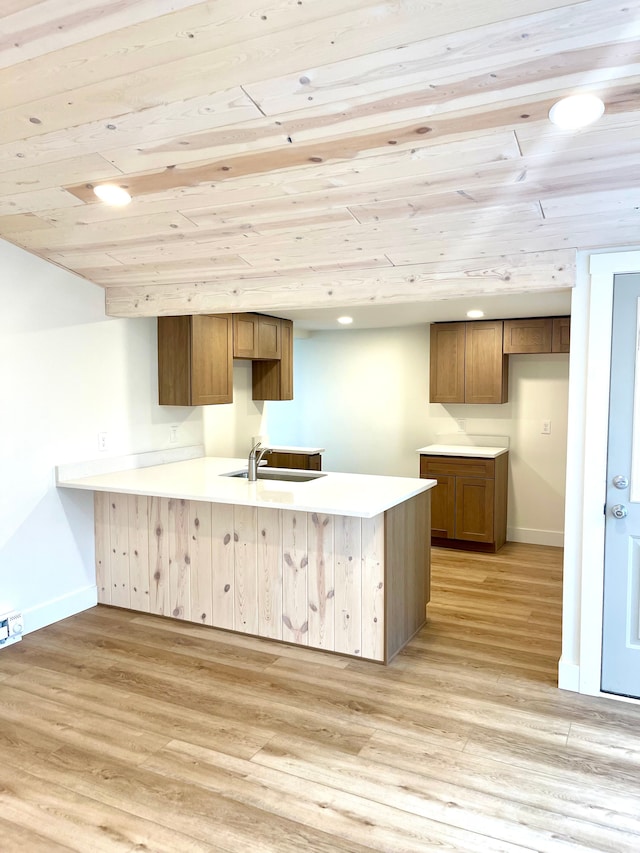 kitchen with light wood finished floors, a peninsula, baseboards, and a sink