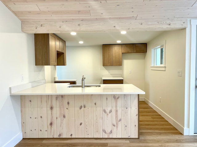 kitchen with baseboards, light wood finished floors, a peninsula, recessed lighting, and a sink