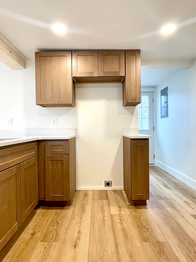 kitchen with brown cabinetry, baseboards, light countertops, and light wood-style floors