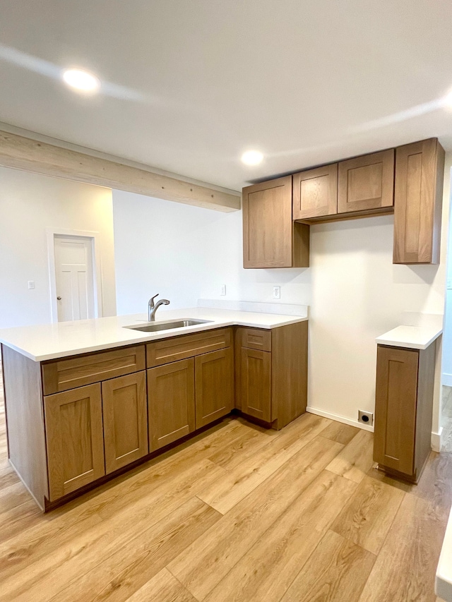 kitchen featuring brown cabinets, light wood finished floors, a sink, a peninsula, and light countertops