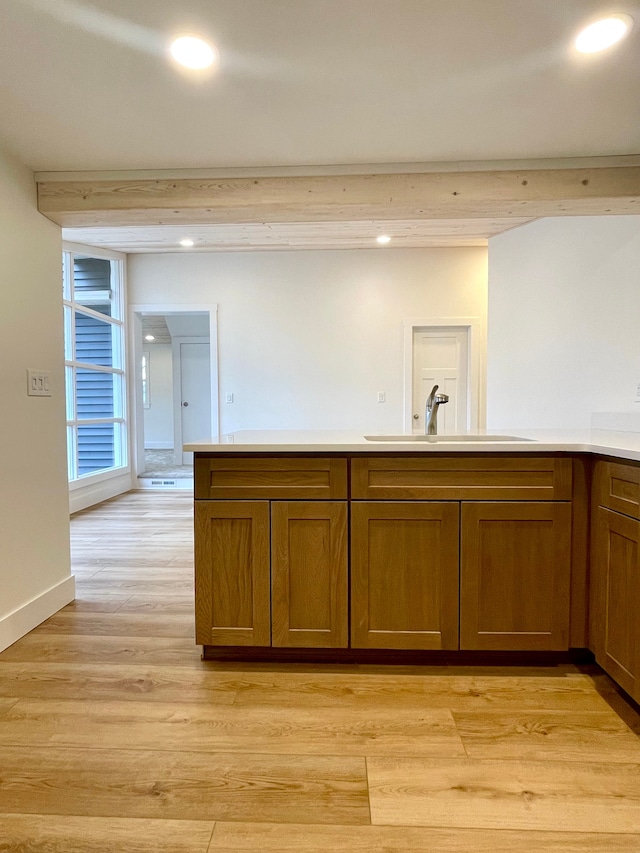 kitchen with light wood-style flooring, a sink, recessed lighting, brown cabinetry, and light countertops