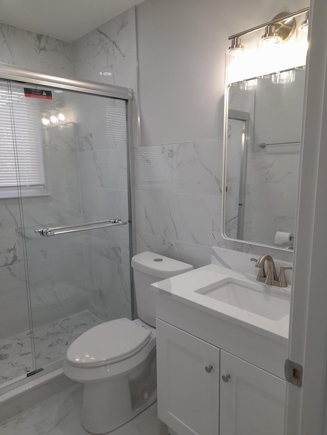 bathroom featuring toilet, marble finish floor, a marble finish shower, tile walls, and vanity