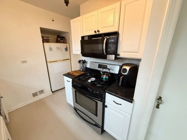 2126 Pierce St, Flint, MI 48503 - kitchen featuring visible vents, black microwave, dark countertops, stainless steel gas range, and freestanding refrigerator
