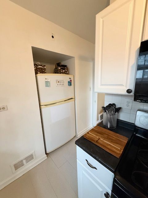 2126 Pierce St, Flint, MI 48503 - kitchen with visible vents, freestanding refrigerator, dark countertops, white cabinets, and range