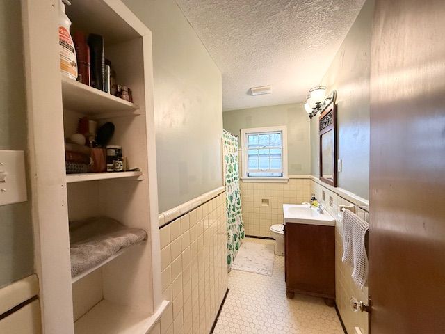 2126 Pierce St, Flint, MI 48503 - full bathroom with wainscoting, vanity, toilet, a textured ceiling, and tile walls