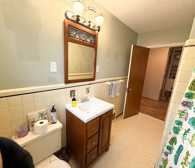 2126 Pierce St, Flint, MI 48503 - bathroom with a textured ceiling, tile walls, vanity, a wainscoted wall, and toilet