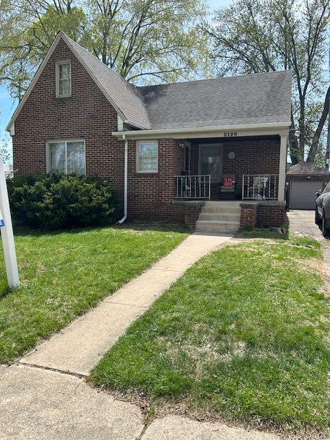 2126 Pierce St, Flint, MI 48503 - view of front of property featuring a porch, a garage, a front lawn, and brick siding