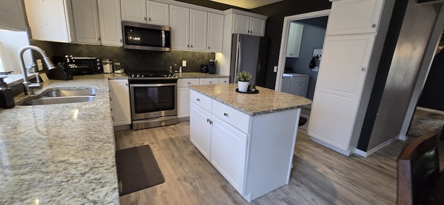 kitchen featuring light wood-style flooring, a sink, stainless steel appliances, white cabinetry, and a center island