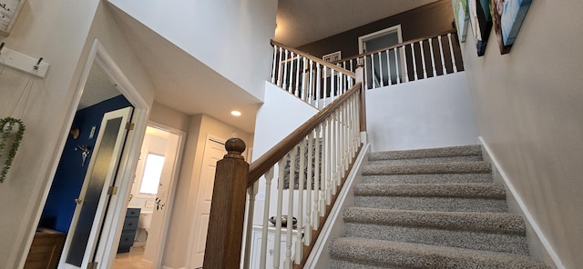 staircase with a high ceiling, recessed lighting, and baseboards