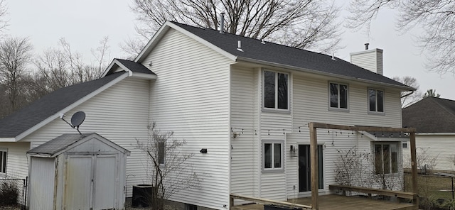 rear view of property with central air condition unit, a wooden deck, a chimney, an outbuilding, and a storage unit