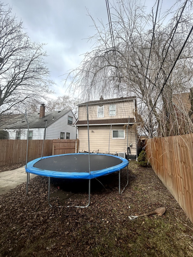 rear view of house featuring a trampoline and a fenced backyard