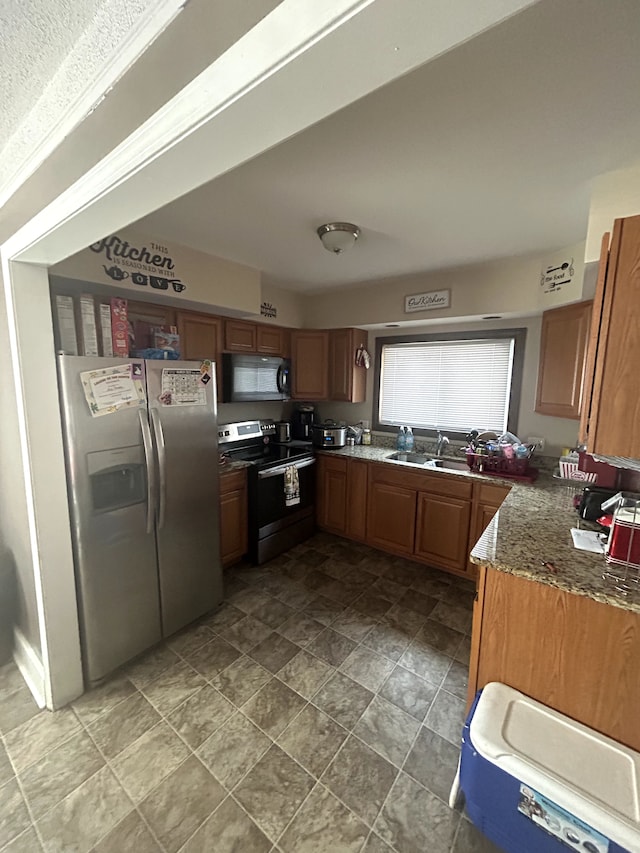 kitchen featuring dark stone countertops, brown cabinets, appliances with stainless steel finishes, and a sink