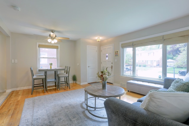 living area featuring light wood-style flooring, a ceiling fan, and baseboards