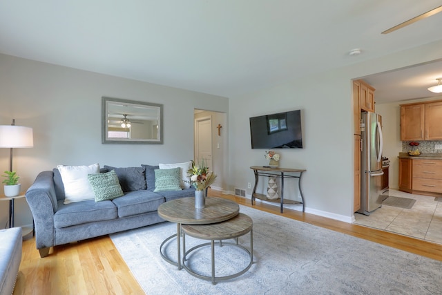 living room with light wood-type flooring, baseboards, and ceiling fan