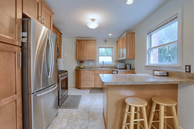 kitchen featuring appliances with stainless steel finishes, a peninsula, a sink, tasteful backsplash, and a breakfast bar