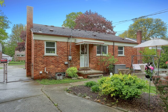 back of house with a gate, a chimney, brick siding, and fence