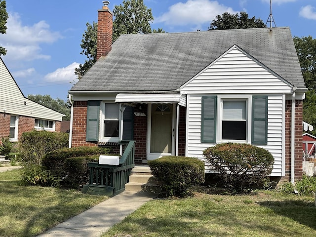 view of front of home with a front yard, brick siding, roof with shingles, and a chimney