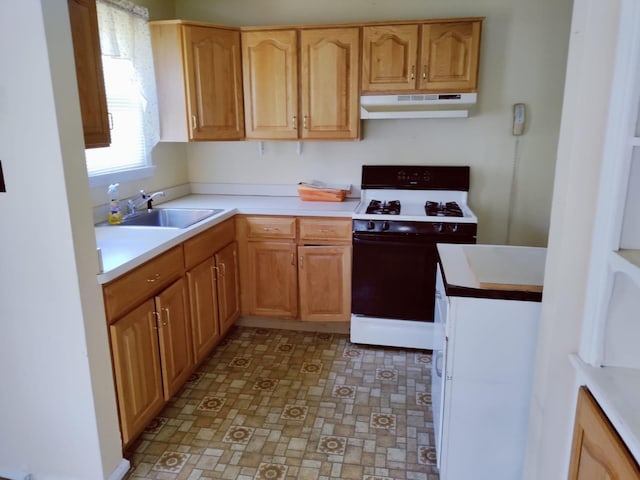 kitchen featuring light countertops, gas range oven, under cabinet range hood, and a sink