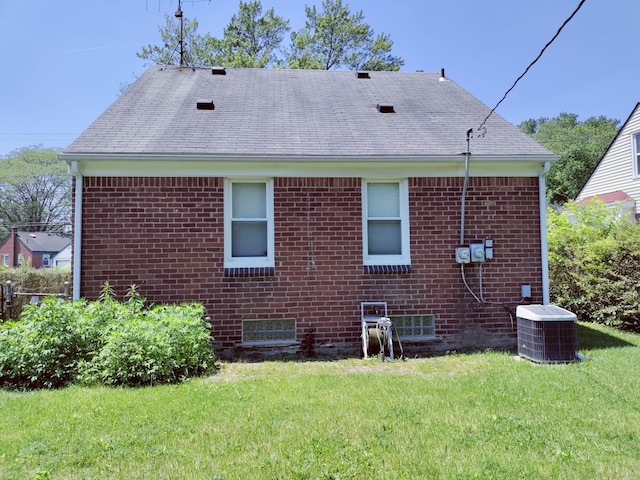 back of property featuring central air condition unit, a yard, brick siding, and a shingled roof