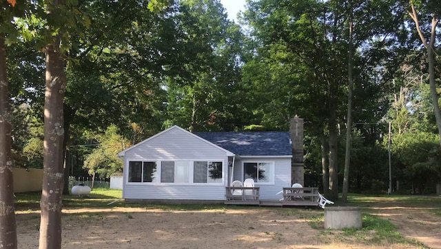 view of front of house featuring a deck, fence, a shingled roof, and a chimney