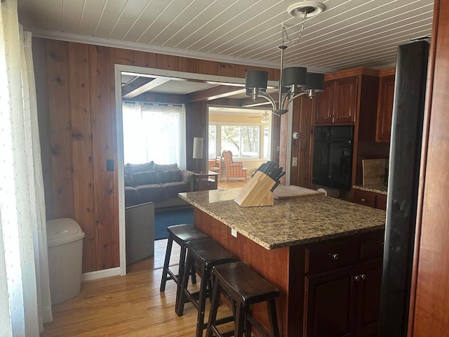 kitchen featuring black oven, crown molding, open floor plan, a kitchen bar, and light wood-style flooring