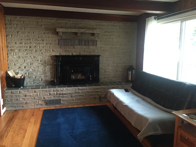 living room with wood finished floors, visible vents, brick wall, beam ceiling, and a brick fireplace