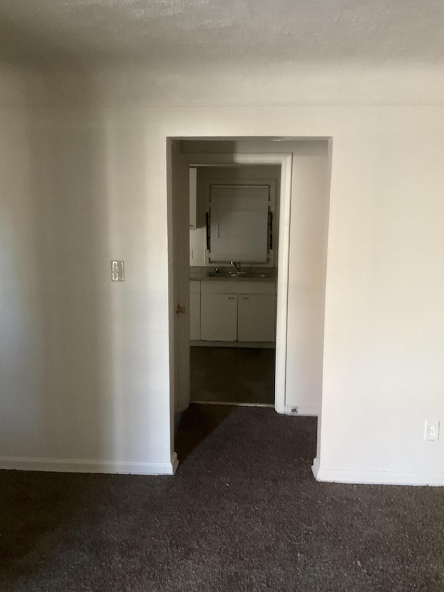 hallway featuring a sink, baseboards, and dark carpet