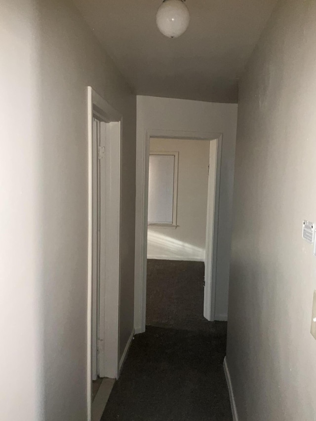 corridor with baseboards and dark colored carpet