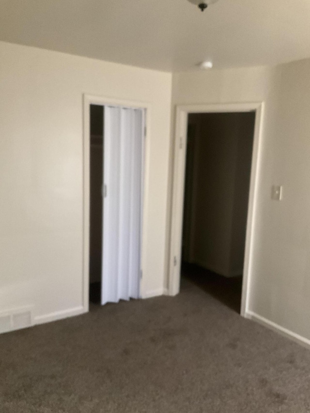 unfurnished room with visible vents, baseboards, and dark colored carpet