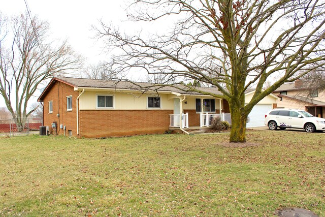 ranch-style home featuring covered porch, a front yard, a garage, brick siding, and central AC unit