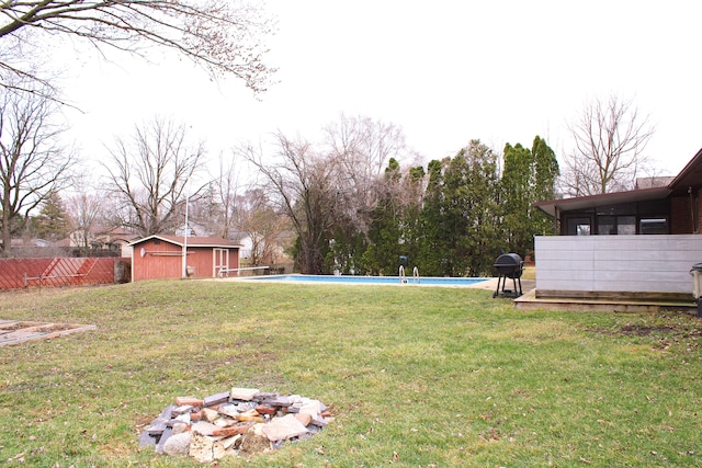 view of yard with an outbuilding, a fenced in pool, a fire pit, and fence
