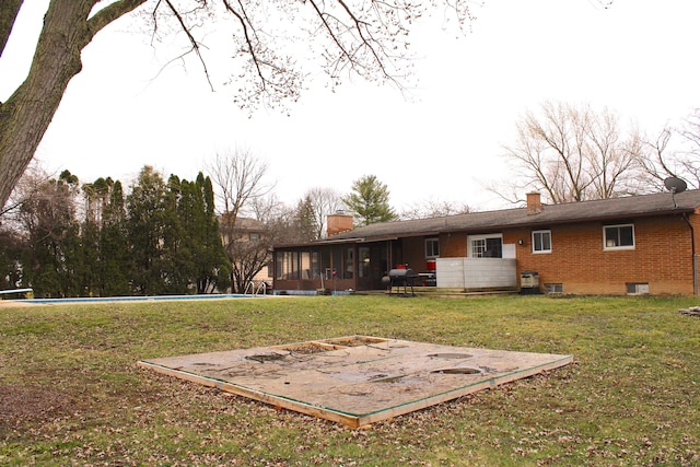 back of property with a lawn, brick siding, a sunroom, and a chimney