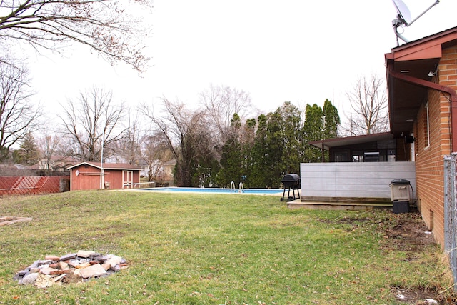 view of yard featuring an outdoor pool, a storage unit, an outbuilding, and fence