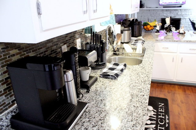kitchen featuring a sink, light stone counters, tasteful backsplash, wood finished floors, and white cabinetry
