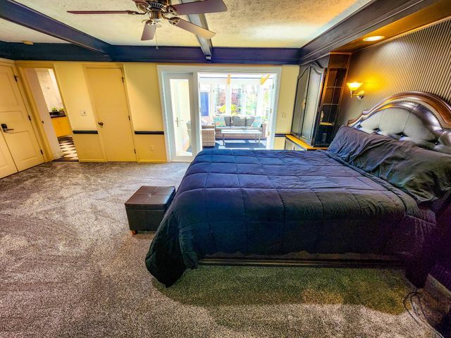 bedroom featuring carpet floors, beamed ceiling, a ceiling fan, and access to exterior
