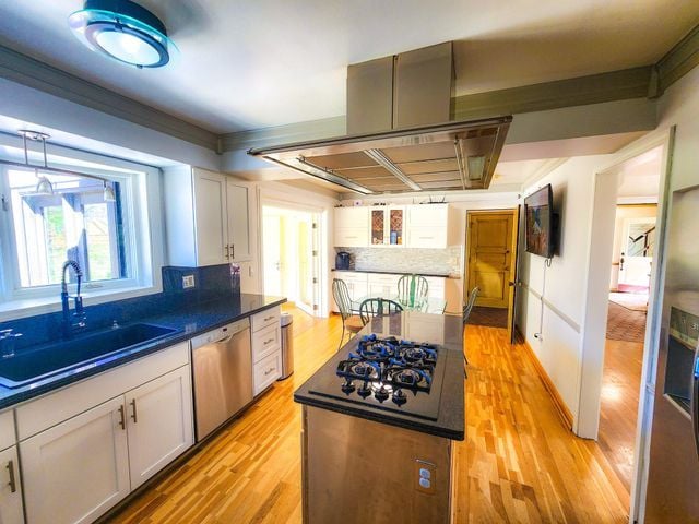 kitchen featuring dark countertops, a sink, light wood finished floors, dishwasher, and black gas cooktop