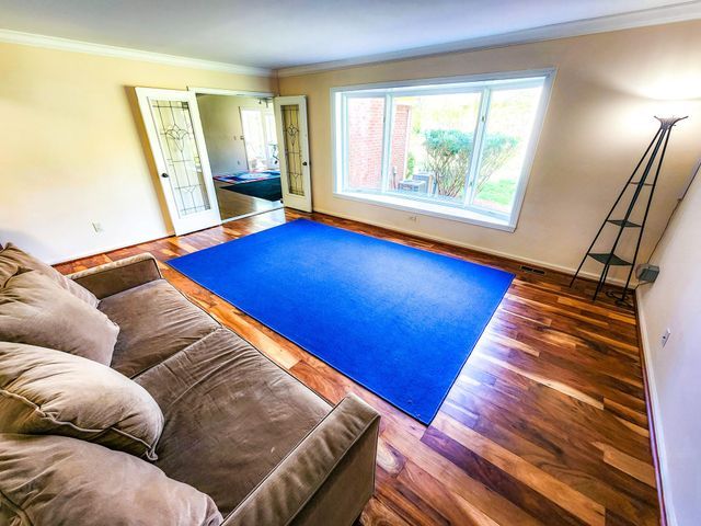 living area featuring crown molding, baseboards, wood finished floors, and visible vents
