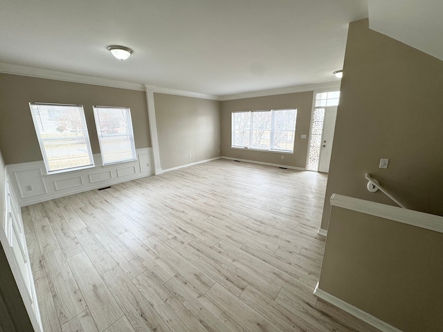 unfurnished living room with a decorative wall, wood finished floors, a wainscoted wall, and ornamental molding