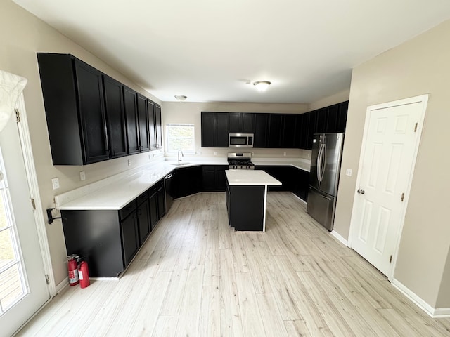 kitchen featuring a sink, a kitchen island, dark cabinetry, light wood-style floors, and appliances with stainless steel finishes