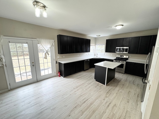 kitchen featuring a kitchen island, dark cabinets, light wood-style floors, stainless steel appliances, and a sink