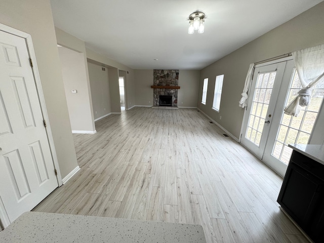 unfurnished living room with a stone fireplace, french doors, baseboards, and light wood finished floors