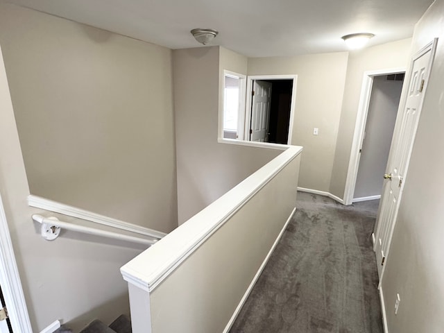 corridor with an upstairs landing, baseboards, and dark colored carpet