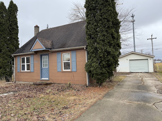 bungalow-style house featuring a shingled roof, a detached garage, a chimney, an outdoor structure, and driveway