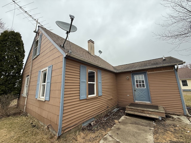 back of house with a chimney and roof with shingles