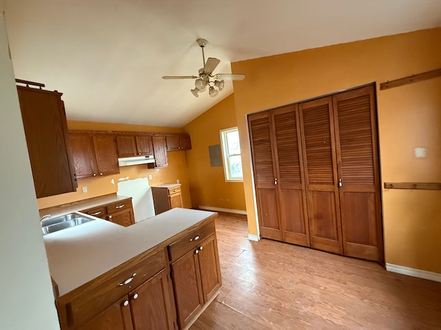 kitchen featuring light wood finished floors, under cabinet range hood, brown cabinets, a ceiling fan, and a sink